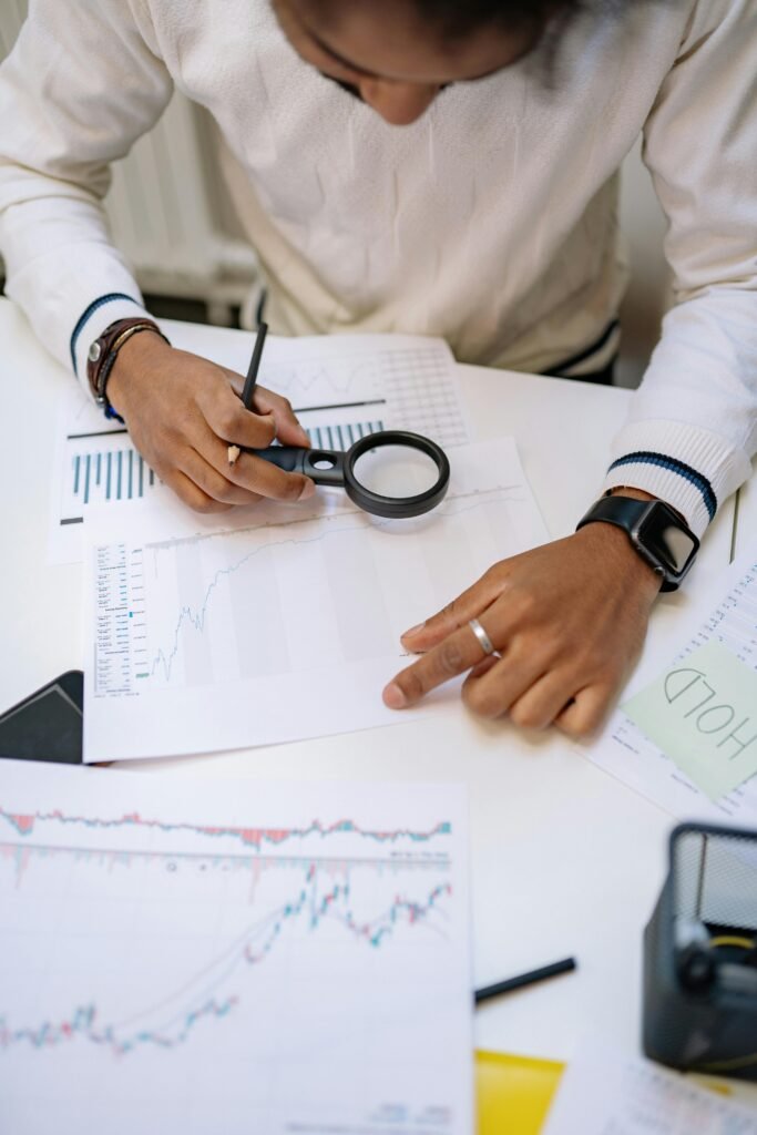 A person analyzing business charts with a magnifying glass, focusing on financial paperwork.