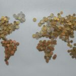 Creative world map made from assorted coins on a solid gray backdrop, symbolizing global finance.